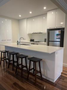 a kitchen with a large white counter with four bar stools at Stylish 4 Bedroom Urban Retreat in Wagga Wagga