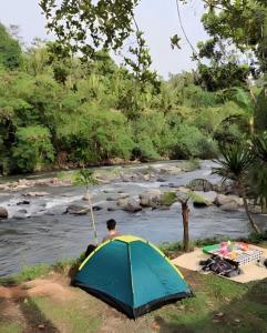 a man sitting next to a tent next to a river at Exorcism Camp in Bukittinggi