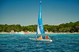 two people on a small sail boat in the water at Pine Beach Mobile homes all inclusive in Pakoštane