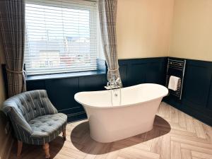 a bath tub in a bathroom with a chair and a window at Harbour Way Cottage in Seahouses