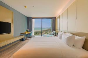 a bedroom with a large white bed with a large window at Awaken Da Nang Hotel in Danang