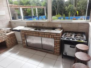 a kitchen with a stove and a sink and two stools at Chácara Rancho da Felicidade in Mogi das Cruzes