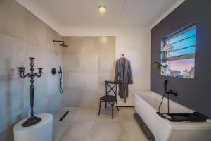 a bathroom with a tub and a chair in it at Leadwood House in Jeffreys Bay