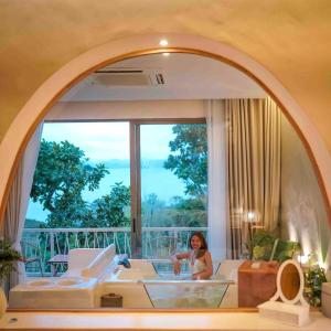 Le La Lake Resort and Spa في كانغ كاتشان: امرأة جالسة في غرفة المعيشة مع نافذة كبيرة