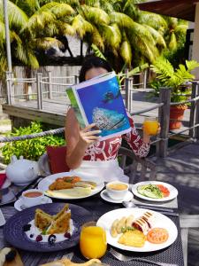 a woman holding a book while sitting at a table with food at DoubleTree by Hilton Seychelles Allamanda Resort & Spa in Takamaka