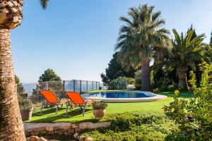 un patio con 2 sillas y una piscina con palmeras en Villa Sabine - PlusHolidays, en Calpe