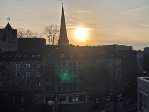 einen Sonnenuntergang über einer Stadt mit Kirchturm in der Unterkunft FEWO FAUBEL Mülheim Forum City 60 m2 in Mülheim an der Ruhr