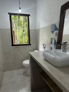 uma casa de banho com um lavatório, um WC e uma janela. em Chalé da Mata Trancoso em Trancoso