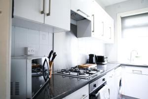 a kitchen with white cabinets and a stove top oven at Glasgow, 3 Bed Close to City Centre, Free Street Parking in Maryhill