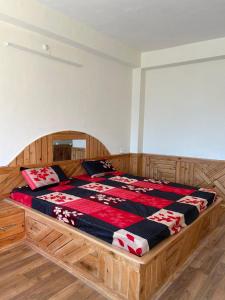 a wooden bed with a red and black blanket on it at Aarav Homestay in Kalpa