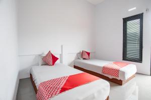 2 camas en una habitación blanca con almohadas rojas y blancas en OYO 93476 Owo Guest House Syariah, en Jambi