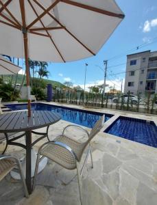 uma mesa e cadeiras com um guarda-sol ao lado de uma piscina em Quarto em floripa em Florianópolis