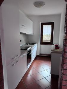 una cucina con armadi bianchi e pavimento piastrellato rosso di Casa Stefy a Mezzolago