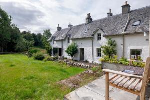 uma casa branca com um quintal com um banco em Refurbished Highland Lodge in Spectacular Scenery em Pitlochry