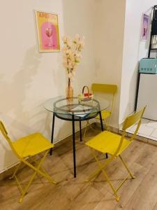 einen Glastisch mit zwei gelben Stühlen und eine Vase mit Blumen in der Unterkunft cocooning modern design studio in Avesnes-sur-Helpe