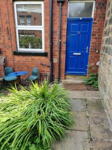 eine blaue Tür in einem Backsteingebäude mit zwei Stühlen in der Unterkunft Blue Door Cottage in Meanwood