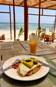 a plate with a sandwich and a glass of orange juice at HA Beach Hotel Zanzibar in Jambiani