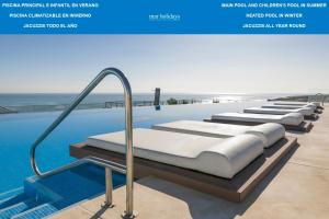 a pool with a row of beds next to the ocean at Infinity View by Mar Holidays - Arenales del Sol in Arenales del Sol