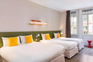 2 łóżka w pokoju hotelowym z żółtymi poduszkami w obiekcie Matabi Hotel Toulouse Gare by HappyCulture w Tuluzie