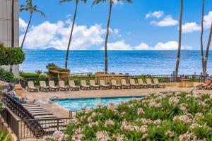 a pool with chairs and the ocean in the background at Sugar Beach Resort in Kihei