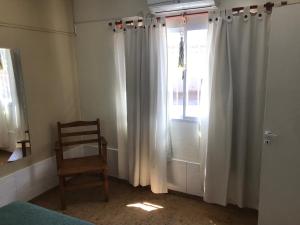 a bedroom with a chair and a window with curtains at Complejo El Pinar in Las Grutas