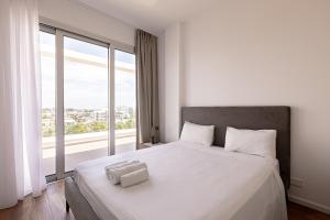 Schlafzimmer mit einem weißen Bett und einem großen Fenster in der Unterkunft YAMAS Urban Living Sunny Pool Penthouse in Limassol