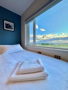 a bedroom with a white bed with a large window at Cabañas Los Coihues in Puerto Natales