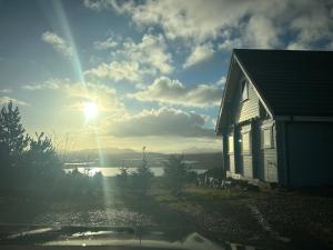 a house next to a lake with the sun in the sky at Sundown Cottages in Leurbost