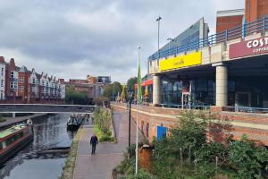 a man walking down a sidewalk next to a river at 2 Bedroom Apartment Central Birmingham City Centre ( Parking ) in Birmingham