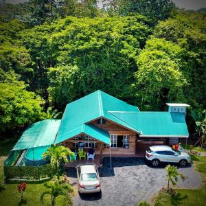 ein Haus mit grünem Dach und zwei Autos geparkt in der Unterkunft Cabaña Río Blanco Guapiles Costa Rica in Guápiles