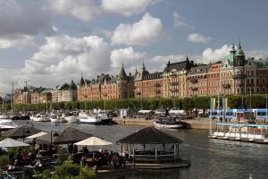 eine Gruppe von Tischen und Sonnenschirmen neben einem Fluss mit Booten in der Unterkunft Lägenhet i centrala Stockholm in Stockholm