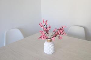 a white vase with pink flowers on a table at Los Arenales Agaete in Agaete