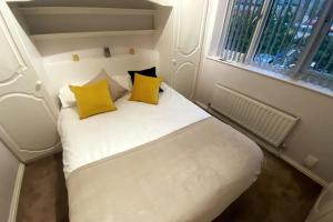 a small room with a white bed with yellow pillows at Boss Breaks-Luton in Luton