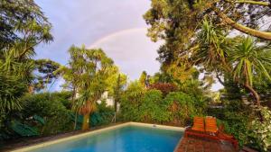 a pool with two chairs and a rainbow in the background at Casa con piscina en Sierra de los Padres in Mar del Plata