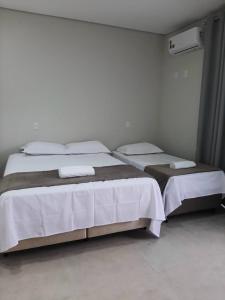 um quarto com 2 camas com lençóis brancos e almofadas em Pousada Lobo Guará em São João Batista do Glória