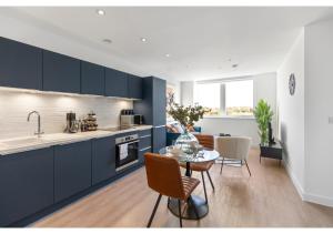 cocina con armarios azules, mesa y sillas en Beckenham Beauty: Modern 1-Bedroom Abode en Beckenham