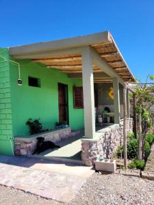 ein grünes Haus mit einer Katze unter einer Veranda in der Unterkunft Cabañas Kurmi in Humahuaca