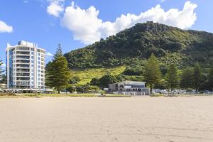 a beach with a building and a mountain in the background at Oceanside Sunset Views in Mount Maunganui