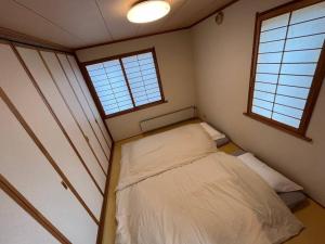 een kleine kamer met een bed en 2 ramen bij Kitamachi Home in Higashikawa