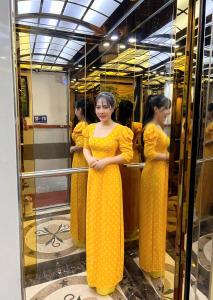 Gia Hân Hotel في مدينة هوشي منه: امرأة ترتدي ثوب أصفر تقف أمام المرآة