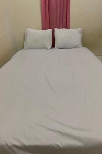 a white bed with two pillows and a pink curtain at OYO Life 93259 Kos Kurnia in Tanjung