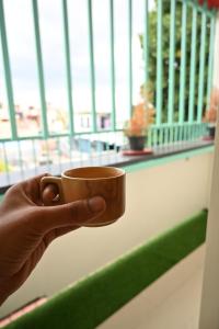 una mano sosteniendo una taza de café frente a una ventana en Hotel SY Comforts en Bangalore
