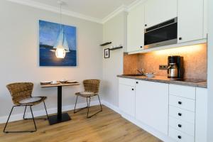 uma cozinha com armários brancos e uma mesa e cadeiras em Am Dorfteich 5, App 18 em Wenningstedt