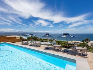 a swimming pool with tables and umbrellas and the ocean at Plett Quarter Apartments in Plettenberg Bay