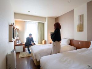 Hotel Resol Ikebukuro في طوكيو: امرأة تقف بين سريرين في غرفة الفندق