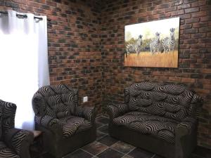 een kamer met 2 stoelen en een schilderij van zebra's bij Kruger Wild Dog Inn in Marloth Park