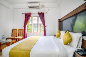 1 dormitorio con 1 cama blanca grande con almohadas amarillas en FabHotel Abrigo Residency en Munnar