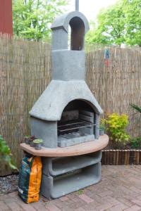 a stone oven in a backyard with a fence at Zentopia: vakantiehuis met wellness en meer. in Hulshorst
