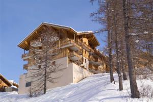 un bâtiment sur une colline enneigée avec des arbres dans l'établissement Madame Vacances Les Balcons Des Airelles, aux Orres