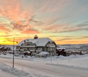 un grand bâtiment dans la neige avec un coucher de soleil dans l'établissement Gjestegaarden Leiligheter, à Beitostøl